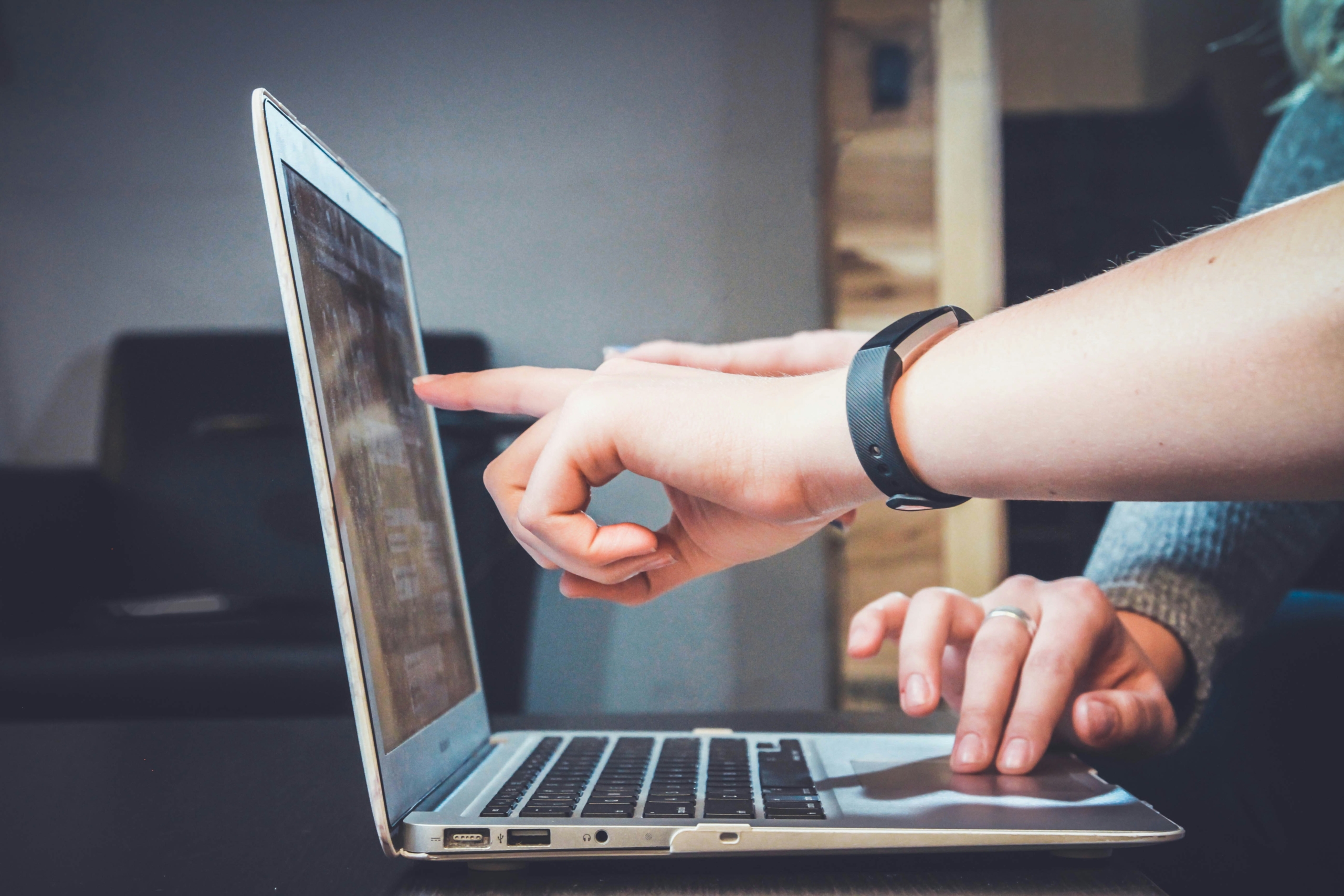 An athlete wearing a fitness tracker pointing at data on a laptop screen while drafting a race report and post-race debrief.