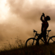 Silhouette of a cyclist drinking from a water bottle on a grassy hill under a dramatic sky, illustrating a personalized fueling and hydration strategy for endurance athletes.