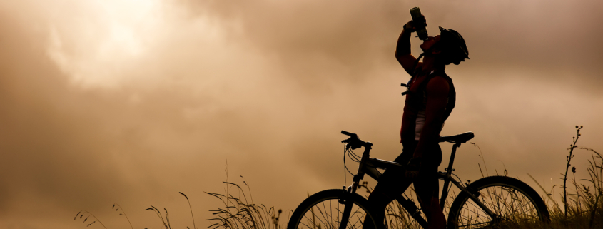 Silhouette of a cyclist drinking from a water bottle on a grassy hill under a dramatic sky, illustrating a personalized fueling and hydration strategy for endurance athletes.