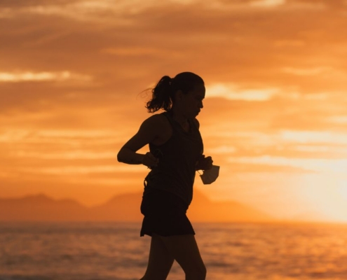 Silhouette of a female endurance athlete running on the beach at sunset, illustrative of managing iron deficiency in runners.