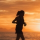 Silhouette of a female endurance athlete running on the beach at sunset, illustrative of managing iron deficiency in runners.