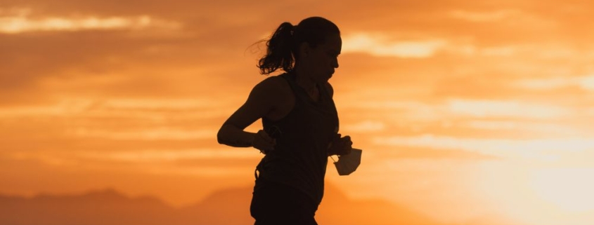 Silhouette of a female endurance athlete running on the beach at sunset, illustrative of managing iron deficiency in runners.
